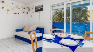 A room with a dining table set for four, a sofa with blue cushions, and a wall decorated with various items. - Mandre Coastal Hideaway (Kolan)