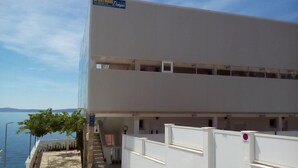 A two-story building with a sign indicating it is an apartment complex. There is a staircase leading to the entrance, and a view of the sea in the background. - Comfortable Holiday Home in Okrug Gornji (Okrug)