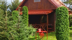 Une cabane en bois avec un toit rouge, entourée d’une végétation bien entretenue, et une chaise rouge placée au premier plan.