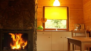L’intérieur d’un chalet accueillant, avec une cheminée en pierre, des murs en bois, une fenêtre offrant une belle vue et un petit coin cuisine.