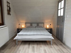 A single bed in a room with white walls and wooden flooring. There are two bedside tables with lamps, a radiator, and a window with a view.