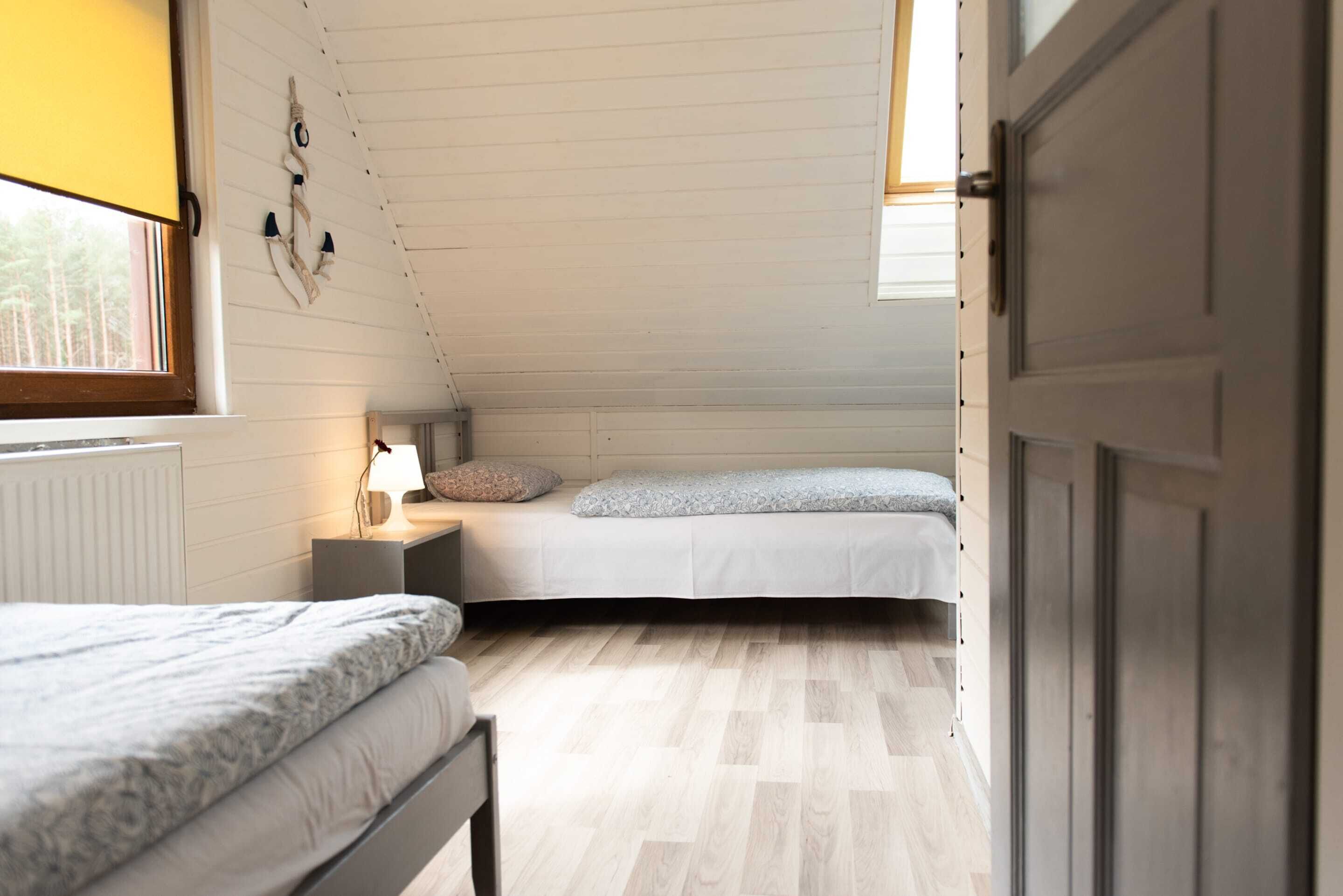 A small, cozy attic bedroom with two beds, a window, and a door.