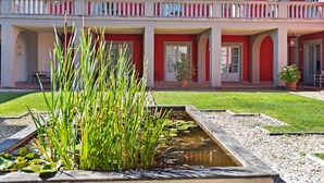 A building with a red facade, multiple balconies, and a small pond with water plants. - Garden & Wine Country Stay (Rignano sull'Arno)