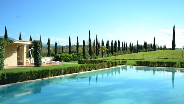 A swimming pool with a clear blue surface, surrounded by neatly trimmed hedges and tall cypress trees. - Garden & Wine Country Stay (Rignano sull'Arno)
