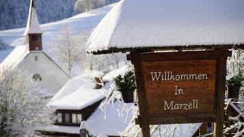 A wooden sign with "Willkommen In Marzell" written on it, surrounded by snow-covered trees and buildings.