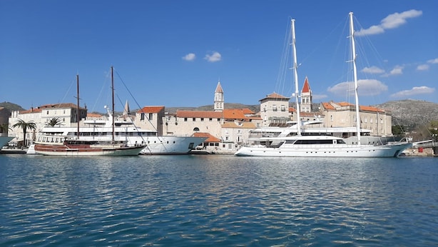 Ein Yachthafen mit mehreren dort vertäuten Yachten, ein historisches Gebäude mit einem Turm und ruhigem Wasser.