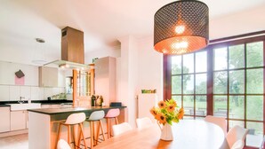 A modern kitchen with a central island, bar stools, a dining table, and a large window with a view of greenery. - Splendid Villa in Vorsen (Gingelom)
