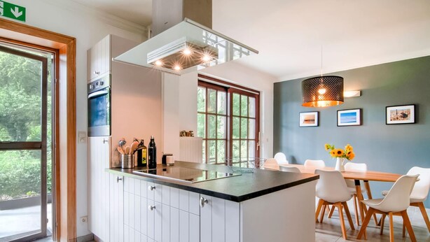 A modern kitchen with a central island, white cabinetry, and a dining area with a wooden table and chairs. - Splendid Villa in Vorsen (Gingelom)