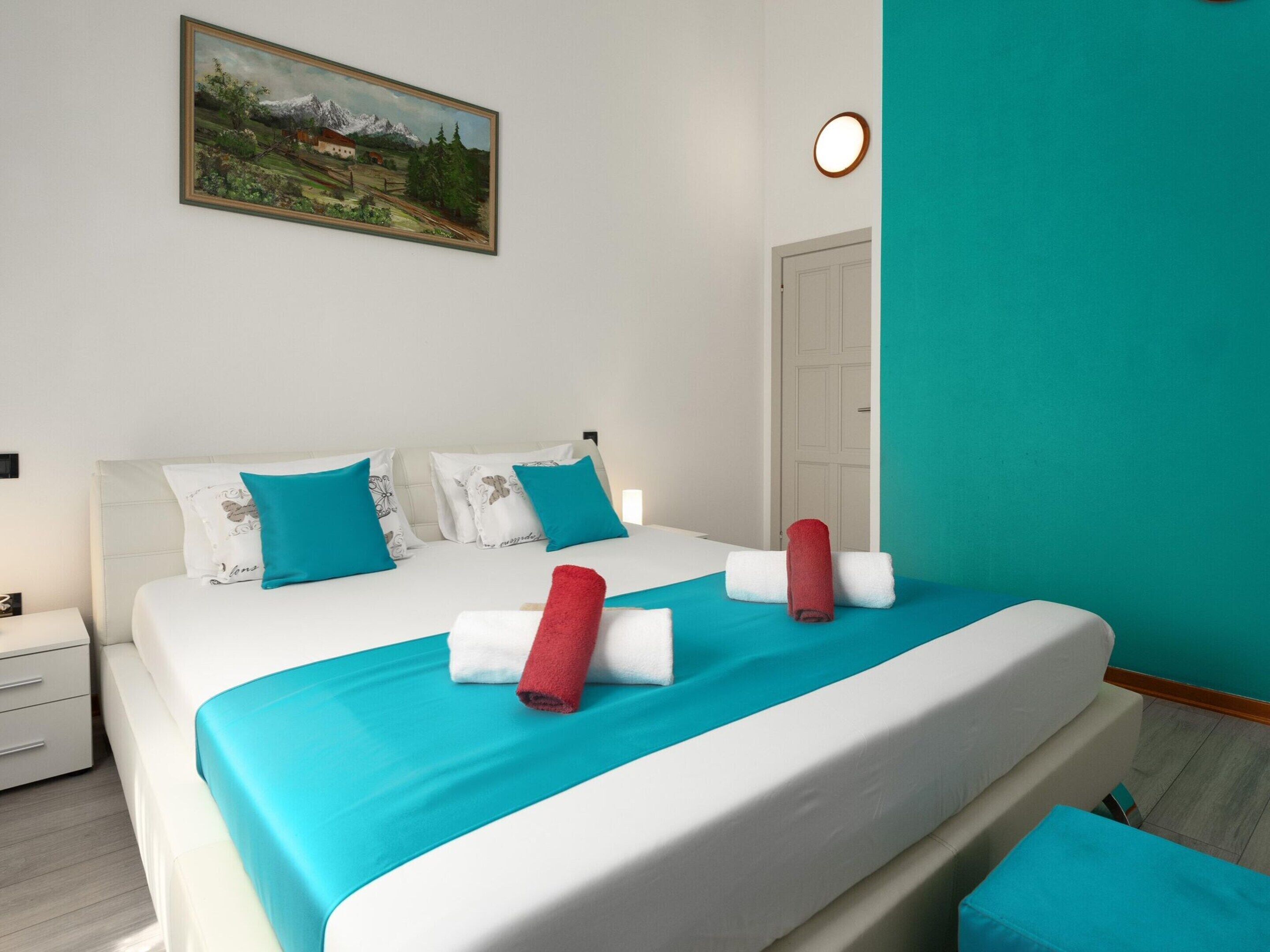 A hotel room with a bed, a nightstand, a painting on the wall, and a door.