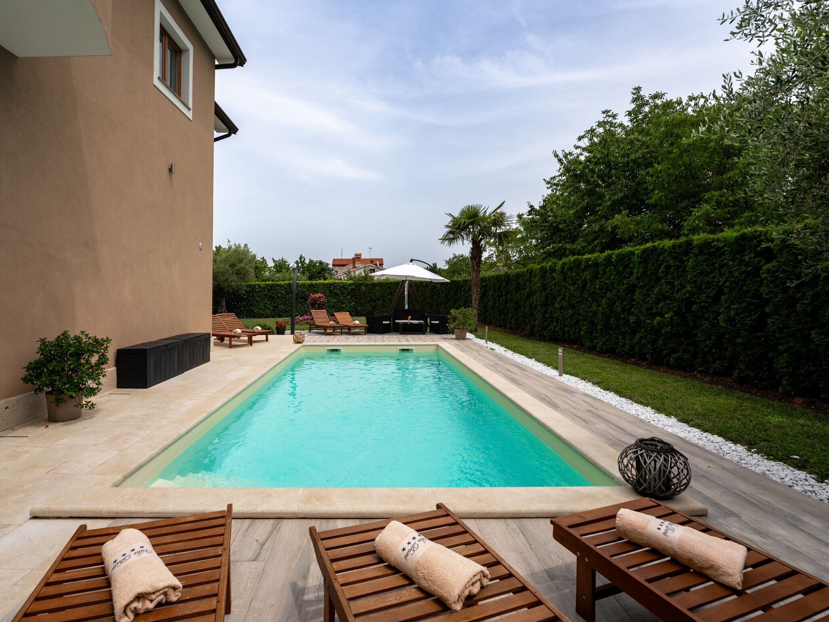 A rectangular swimming pool with lounge chairs and towels, surrounded by a landscaped garden and a hedge.