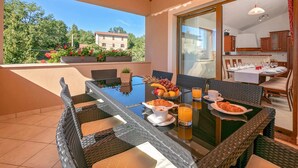 Zona de menjador amb taula de vidre, cadires de vimetla i articles per a l'esmorzar, com ara croissants, fruita i suc d'aranja.