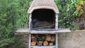 A stone-built outdoor oven with a thatched roof, surrounded by greenery. - Seaside Bliss in Mandre (Kolan)