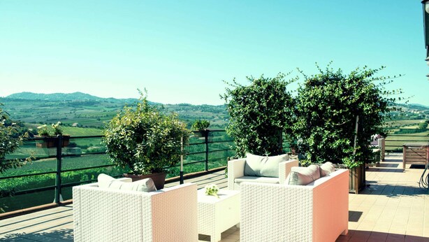 A terrace with wicker furniture and potted plants, overlooking a scenic landscape. - Apartment Amidst Vineyards & Blue Skies (Coriano)
