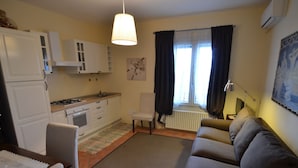 A compact living space with a kitchenette, a sofa, a dining table, and a window with curtains. - Apartment Amidst Vineyards & Blue Skies (Coriano)