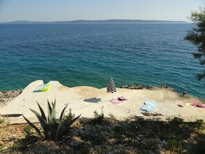 A beach with a clear view of the sea and distant hills. There are several beach umbrellas and towels on the sand.