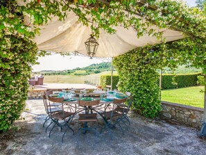 Een terras buiten met een eettafel, omgeven door groen en uitzicht op het landschap.