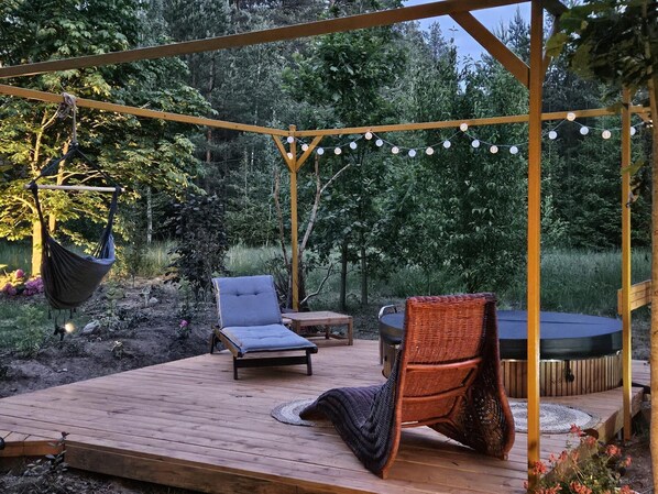 A wooden deck with a swing, two lounge chairs, a wicker chair, and a hot tub.