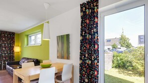 Un moderno salón con comedor, un sofá, una mesa con sillas, una l ámpara y vistas al exterior.