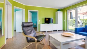 Una sala de estar moderna con un sillón de cuero, una mesa blanca, un sofá azul y un televisor sobre un mueble blanco.