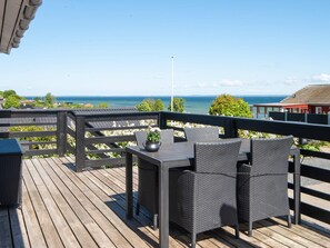 A wooden deck with wicker furniture, a potted plant, and a view of the sea.