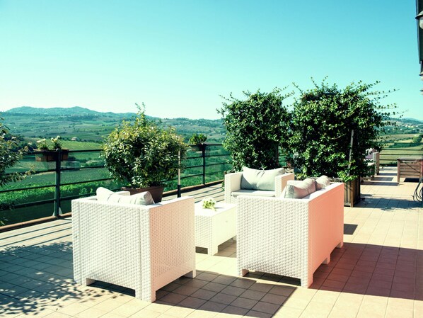 A terrace with wicker furniture and potted plants, overlooking a scenic landscape.