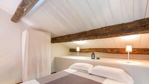 Una camera da letto con un letto, una trave in legno al soffitto, una parete bianca e un comodino con una lampada.