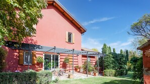 Una casa rossa con un portico coperto, un prato e diverse piante in vaso.