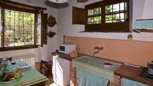 Een keuken met een eettafel gedekt voor twee personen, een magnetron, een spoelbak en een raam met uitzicht op groen.