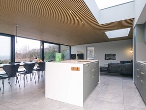 Une cuisine moderne dotée d’un îlot central, d’un coin repas avec des chaises et offrant une vue dégagée grâce à de grandes fenêtres.