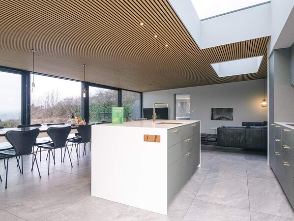 Una cocina moderna con una isla central, ventanas amplias y un comedor con sillas.