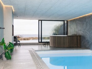 A modern outdoor pool area with a wooden reception desk, large windows, and potted plants. - 5 Star Holiday Home in Ebeltoft (Ebeltoft)