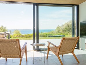 Una habitación moderna con grandes puertas de vidrio, dos sillas de mimbre, una pequeña mesa redonda y vista al mar.