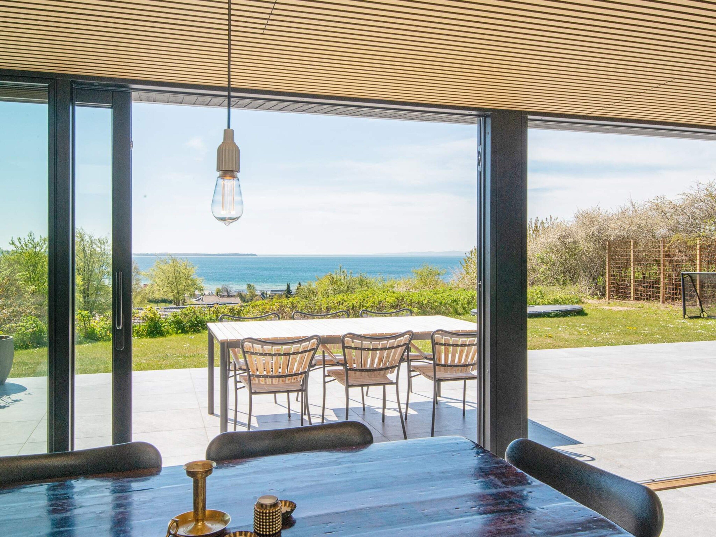 A dining area with a table and chairs, large windows, and a hanging light fixture.