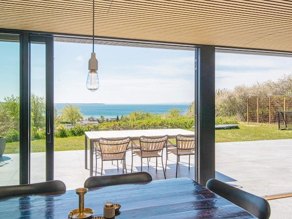 A dining area with a table and chairs, large windows, and a hanging light fixture.