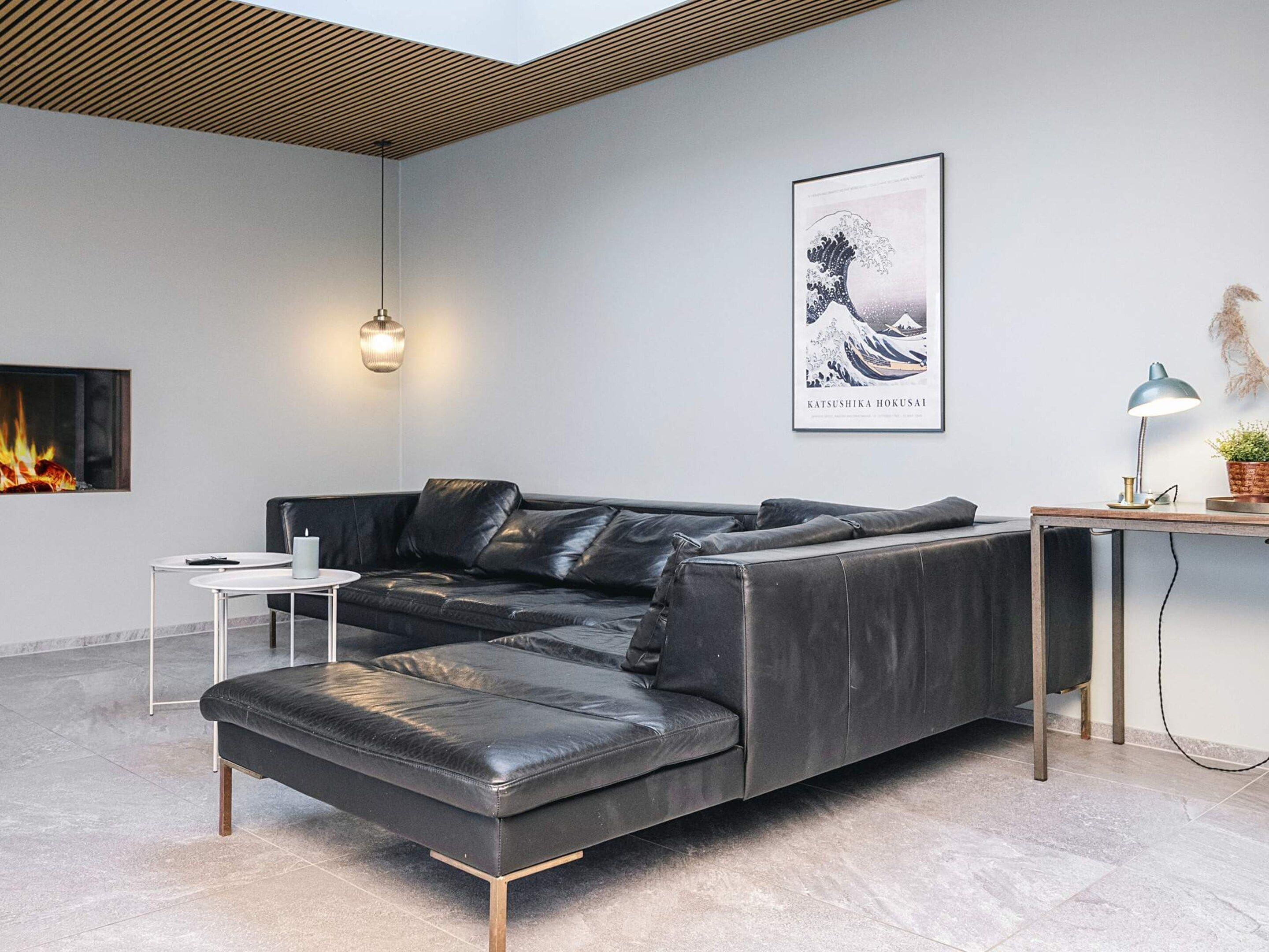 Ein modernes Wohnzimmer mit einem ledernen Ecksofa, einem kleinen weißen Beistelltisch, einem gerahmten Kunstwerk an der Wand und einem Kamin.