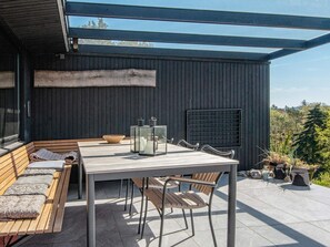 A modern outdoor patio with a wooden bench, a table, and chairs. - 5 Star Holiday Home in Ebeltoft (Ebeltoft)