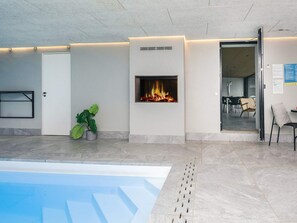 Un área de piscina interior moderna con chimenea integrada, zona de estar y una puerta que da a otro espacio.