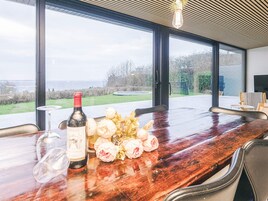 Una mesa de comedor con una botella de vino, copas y flores, con vistas a un paisaje.