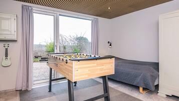 A room with a wooden foosball table, a bed, a guitar, and a window with curtains.