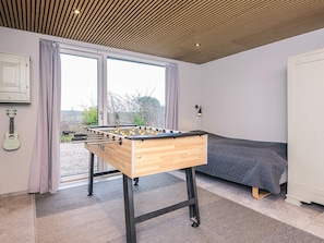 A room with a wooden foosball table, a bed, a guitar, and a window with curtains.