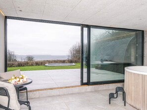 A modern outdoor seating area with a view of the sea, a roundabout, and a glass-enclosed space. - 5 Star Holiday Home in Ebeltoft (Ebeltoft)