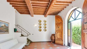 A spacious room with a white sofa, a staircase, a wooden door, and a view of greenery outside. - Poolside Leisure in Empoli Hideaway (Empoli)