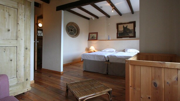 A room with a wooden floor, a bed with white linens, a small table, and a wooden cabinet.