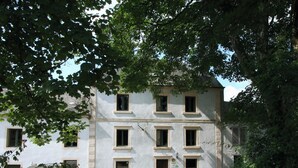 A two-story building with multiple windows and a door, surrounded by trees and gravel.