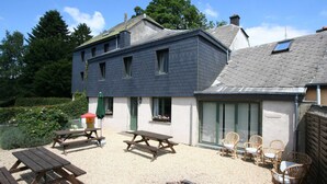 A two-story building with a gravel patio, picnic tables, wicker chairs, and a fire pit.
