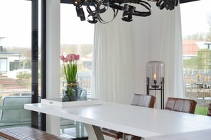 A modern dining area with a white table, brown leather chairs, and a vase with flowers. - Luxury Villa on the Waterfront With Jetty (Zeewolde)