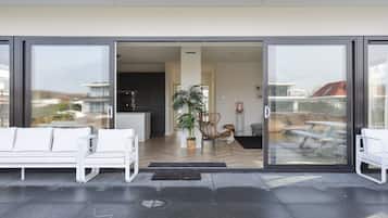 A modern entrance with a glass door, a white sofa, a potted plant, and a wicker chair.