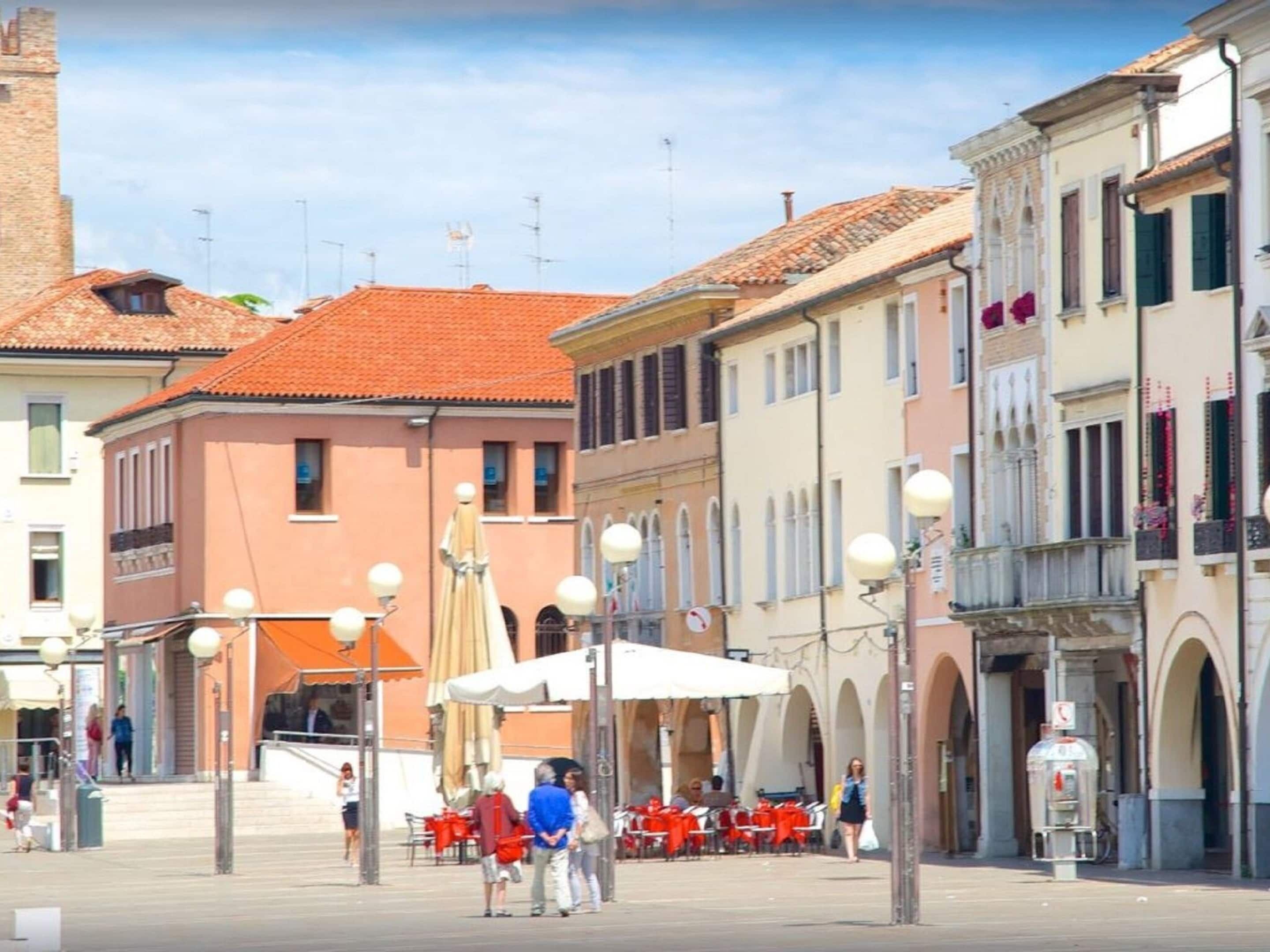 A street with buildings, outdoor seating, and a few people.