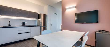 Une cuisine moderne équipée d’un four encastré, d’un réfrigérateur et d’un four à micro-ondes. On y trouve une table à manger avec des chaises, ainsi qu’un téléviseur à écran plat fixé au mur.
