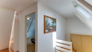 Une pièce avec un plafond en pente, un plancher en bois, une porte blanche, un tableau et une rambarde blanche.